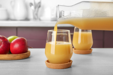 Pouring apple juice from bottle into glass on kitchen table © Africa Studio