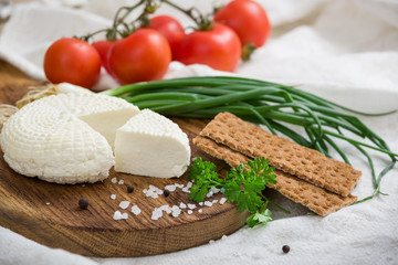 Homemade organic white cheese served with Tomatoes, Basil, onions and crispy bread, herbs and salt on wooden board on the table. Healthy food, snack and eating.