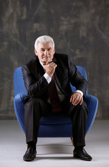 Handsome mature man sitting in armchair on dark background