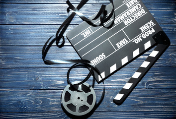 Movie clapper and reel on wooden background, top view
