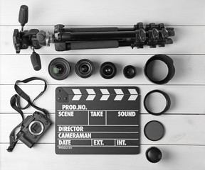 Composition with movie clapper, tripod, camera and different lenses on light background, top view