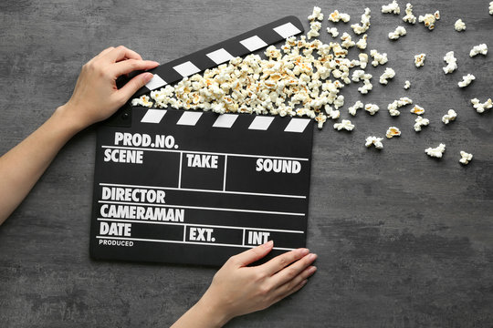 Woman holding movie clapper with popcorn shooting out of it on grey background