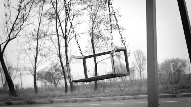 The deserted swing in the park swaying, close-up
