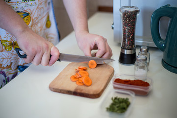 Chef is cutting carrot on a wooden cutting board with sharp knife