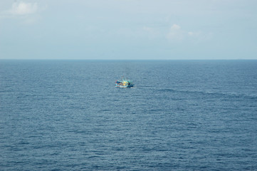 A fishing boat heading out to sea. The sea is calm and the sky pale blue with faint clouds.