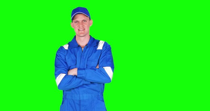 Young Caucasian car mechanic standing in the studio while wearing uniform and smiling at the camera in front of green screen background, shot in 4k resolution