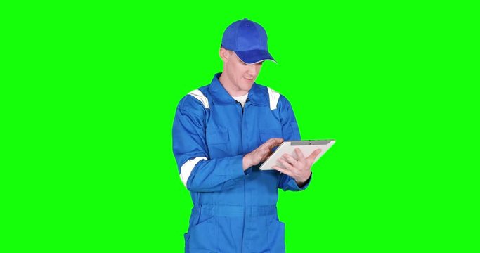 Caucasian car mechanic working with a digital tablet and wearing blue uniform, shot in 4k resolution with green screen background