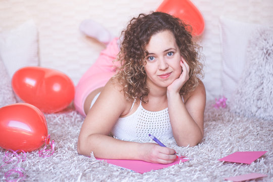 Young beautiful woman smiling and writing a letter for Valentines Day on pink paper.