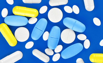 Assorted pharmaceutical medicine pills, tablets and capsules on blue background