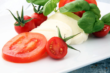 Mozzarella and tomato with basil leaves on a white wooden background