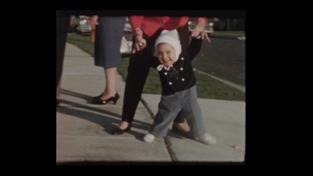 1960 Mother teaching baby son to walk as antique car drives by