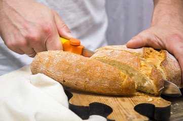 Man's hands cutting bread on the wooden plank.