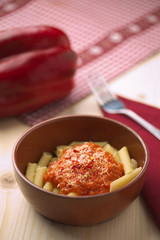 penne alla crema di peperone rosso e parmigiano su tavola in abete con forchetta e tovagliolo rosso.