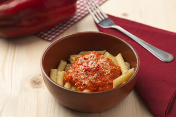 penne alla crema di peperone rosso e parmigiano su tavola in abete con forchetta e tovagliolo rosso.