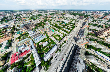 Fototapeta premium Aerial city view with crossroads and roads, houses, buildings, parks and parking lots, bridges. Helicopter drone shot. Wide Panoramic image.