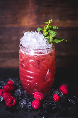 Raspberry cocktail with ice and mint is on the table.