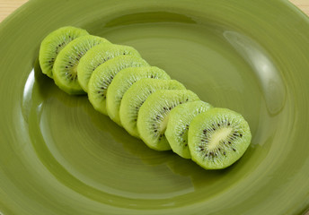 Close up of sliced kiwi fruit on green plate as snack or in preparation to be used as cooking ingredient