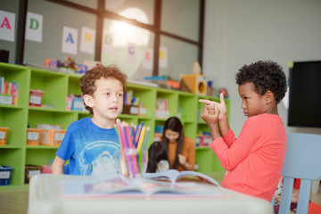 preschool kids kindergarten learning through playing in the playing room together with the teacher watching in background