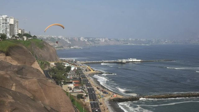 paraglider with a red canopy flies above the coast at miraflores in lima, peru