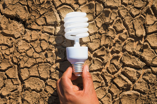 hand holding light bulb on soil arid. concept power solar energy