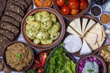 Group food on table: boiled young potatoes, beans, braised cabbage, beet salad with cottage cheese, sliced cheeses, tomato, korean carrot, black bread with seeds, green lettuce leaves