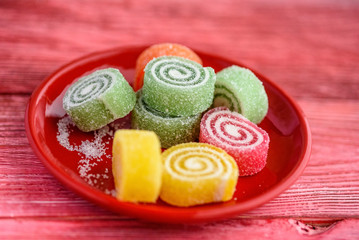 multicolored marmalade on a red plate on a light red wooden background
