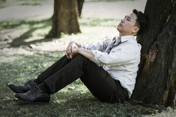 Asian business man failing and serious under tree in the park