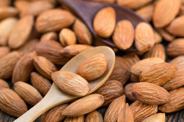 Raw almonds nut on wood spoon and wooden table.