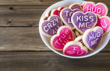 Heart shaped conversation valentine's cookies in white bowl on wooden table.