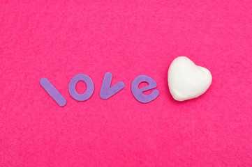 The word love with a white polystyrene heart isolated on a pink background