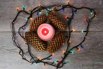 Christmas card. Candle, fir cone, garlands on a wooden background.