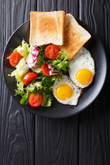 hearty breakfast: fried eggs with fresh vegetable salad and toast close-up. vertical top view