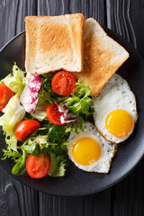 Organic food breakfast: fried eggs with fresh vegetable salad and toast close-up on a plate. vertical top view