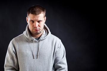 Obraz premium A young, dark-haired, sad-looking man in a sporty gray sweatshirt fell ill with a cold, measured the temperature on a black isolated background. A man holding a thermometer in his mouth