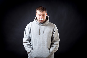 Fototapeta na wymiar A young dark-haired man in a sporting gray sweatshirt fell ill with a cold, he had a nose on a black isolated background. The man in the nose stuffed napkins, so as not to flow snot