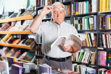 Man 61-67 years old is choosing book for reading in free time