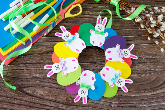 Children's Easter gift wreath with colorful eggs and Easter bunnies.  Paper, scissors, glue on a wooden table.Hand-made. Children's art project for children. Craft for kids.