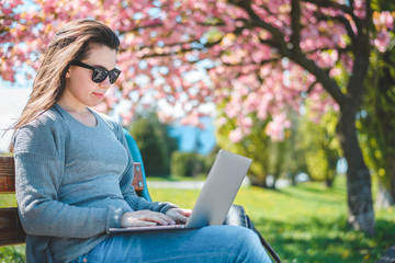 Young beautiful brunette student sit on the banch with laptop