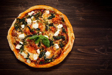 Pizza with feta cheese and spinach on wooden table