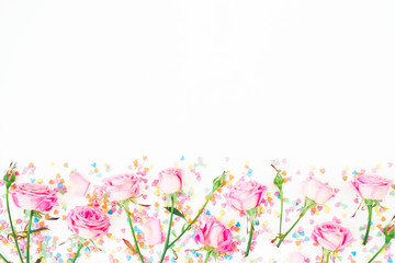 Floral border frame with pink flowers and bright candy confetti on white background. Flat lay, Top view. Roses flower texture
