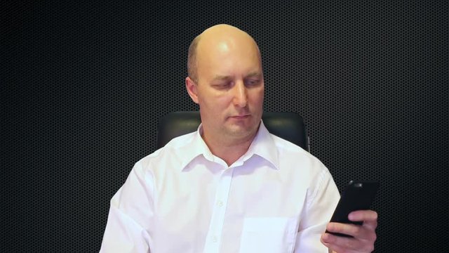 Happy man sitting on chair and texting on phone at techno abstract background.
