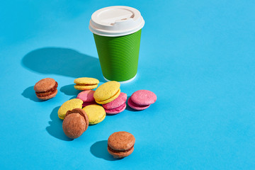 Hot coffee in green paper cup with white lid and macaroons on bl