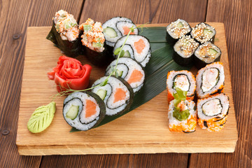 A wooden plate holding different types of sushi pieces. serving sushi and rolls on a wooden plate with ginger and wasabi.
