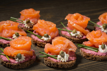 canapé with red fish on rye bread, on a wooden table