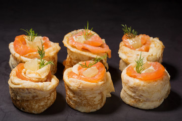 Rolls of pancakes and red fish on a plate of black slate