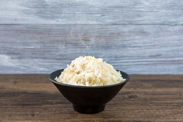 Rice in a black bowl on wood table with various rice in paper box.