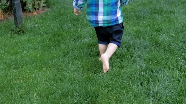 Slow motion video of barefootage 2 years old baby boy running on grass at park