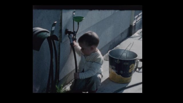 1961  Curious 2 year old little boy plays with waterhose