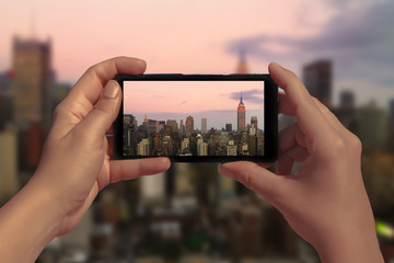 Female hand with mobile phone take picture of midtown of Manhattan on sunset. Plane flies over...