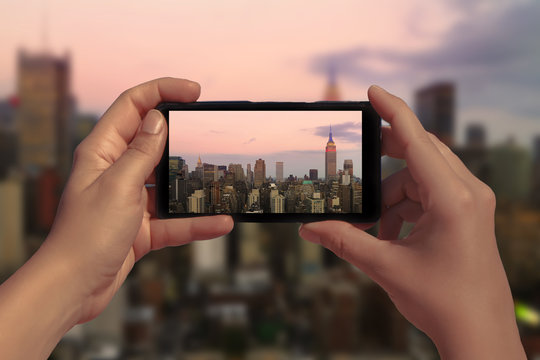 Female hand with mobile phone take picture of midtown of Manhattan on sunset. Plane flies over skyscrapers of New York City, Manhattan.